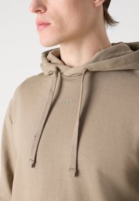 Felpa leggera color beige chiaro con cappuccio regolabile, discreto logo e tessuto morbido e texture. Design semplice e rilassato senza motivi.