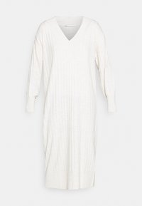 Abito lavorato a maglia color crema con scollo a V, maniche lunghe e texture a costine. Leggermente aderente in vita, termina sopra il ginocchio.