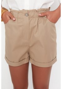 Beige šortky s elastickým pasem, předním knoflíkem, bočními kapsami a ohrnutým lemem. Hladká látka s minimálními švy.