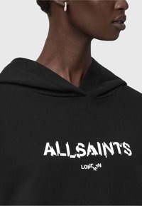 Felpa nera con cappuccio caratterizzata da una grande stampa bianca con la scritta "ALLSAINTS" e "LONDRA." Il tessuto sembra morbido con una vestibilità comoda e un cappuccio con lacci.