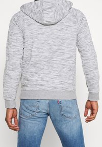 Gray hoodie with a textured, heather pattern. Features a drawstring hood, ribbed cuffs, and waistband. Paired with blue jeans.