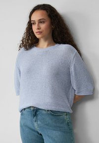 Lichtblauwe gebreide trui met korte mouwen, ronde hals en een losse pasvorm. Zachte textuur, subtiel patroon, gecombineerd met lichtblauwe jeans.