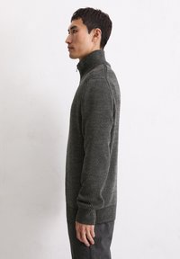 Grauer gerippter Pullover mit hohem Kragen, aus strukturiertem Stoff und langen Ärmeln, kombiniert mit dunkler Hose, von der Seite gezeigt.
