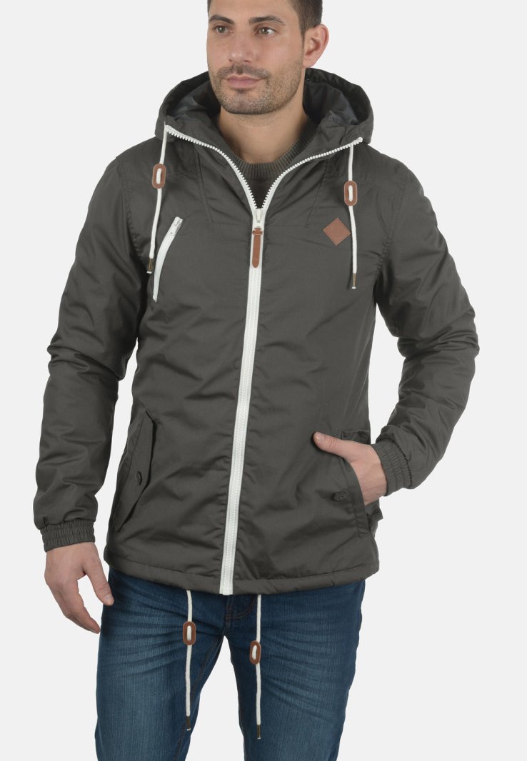 Donkergrijze hooded jack met een witte rits en bruine accenten. Voorzien van elastische manchetten en twee zijzakken. Gemaakt van lichtgewicht stof.