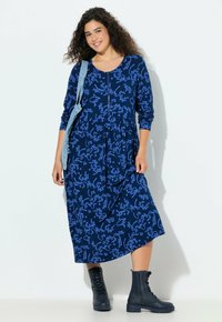 Laivastonsininen mekko, jossa sininen kirjainkuvio, pitkät hihat, levenevä malli ja sivutaskut. Yhdistetty tummiin nyörillisiin sotilastyylisiin saappaisiin.