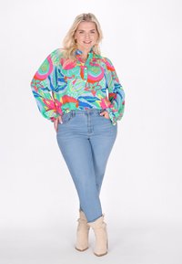 Camicia a maniche lunghe colorata con bottoni, caratterizzata da un motivo floreale e astratto, abbinata a jeans skinny blu chiaro e stivaletti beige alla caviglia.