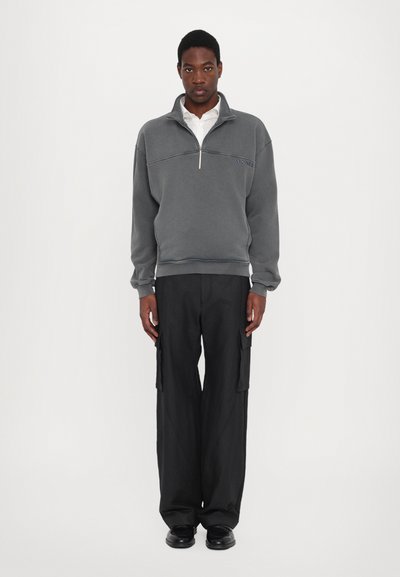 Hanorac gri din fleece cu fermoar, cu guler înalt și manșete ribbate, asortat cu pantaloni cargo negri largi cu buzunare laterale.