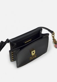 Musta nahkainen käsilaukku, jossa on kultainen neliösolki, kohokuvioitu logo ja ketjuaksentti. Sisäpuolella on useita lokeroita järjestämistä varten.