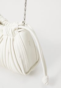 Hvit skinnveske med samlet design, sølvkjede-rem, teksturert overflate og en knyttet detalj på lukkingen.