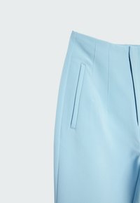 Ljusblå skräddarsydda byxor med en slät yta, som har sidofickor och vertikala veck. Midjan är strukturerad med rena linjer.