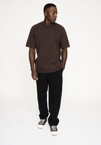 Brun bomulds T-shirt med rund hals og korte ærmer, parret med sorte vide bukser og sneakers med sort og hvidt mønster.