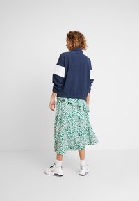 Marinblå fleecejacka med vita axelpaneler, kombinerad med en grön blommig midikjol och vita sneakers. Lätt och sportig design.