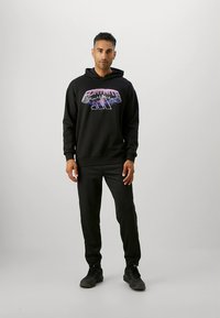 Μαύρο φούτερ με κουκούλα με γραφικό "FORTNITE" σε μωβ, συνδυασμένο με μαύρο παντελόνι φόρμας και μαύρα αθλητικά παπούτσια. Μαλακό ύφασμα με άνετη εφαρμογή.