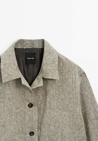 Giacca in lino grigio chiaro con colletto a punte, due grandi bottoni e una tasca sul petto. Le etichette all'interno riportano "Massimo Dutti." Finitura in tessuto testurizzato.