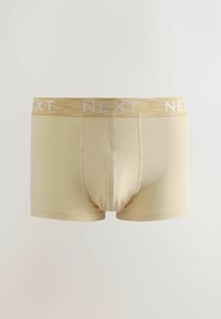 Boxer beige à la texture douce, avec une ceinture élastique jaune clair portant l'inscription "NEXT" en blanc. Conception standard à jambes courtes.