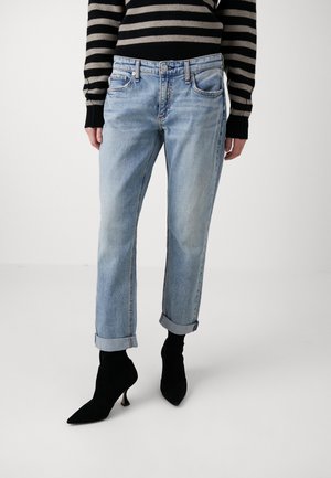 Jeans in denim azzurro chiaro con risvolti, caratterizzati da cinque tasche e chiusura con bottone standard, abbinati a stivaletti neri a punta.