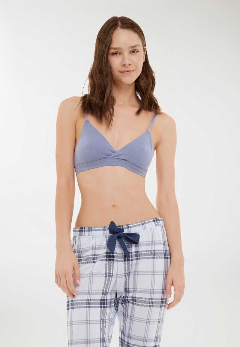 Bralette azzurro con design incrociato e spalline sottili, abbinato a pantaloni del pigiama a quadri bianchi con un fiocco blu navy in vita.