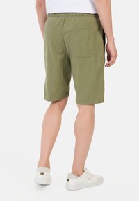 Grønne bomuldsshorts med elastisk talje og baglomme, parret med hvide sneakers. Synlig søm og afslappet pasform.