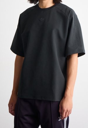 T-shirt de sport noir à manches courtes, doté d'un design sans coutures et de perforations discrètes sur les épaules, rehaussé par un petit logo.