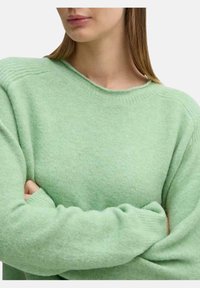 Maglione oversized verde chiaro realizzato in un morbido tessuto testurizzato; presenta un collo a giro e dettagli a coste sui polsini e sulle spalle.