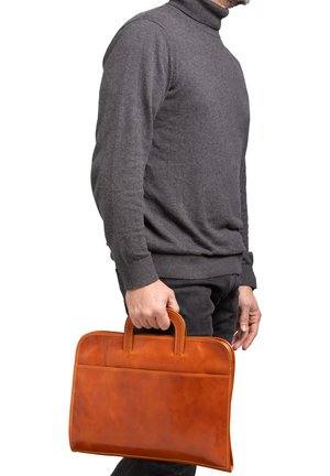 Una valigetta di pelle marrone con due manici, design semplice, texture liscia e un dettaglio di cucitura sottile. Tenuta da una persona che indossa un maglione grigio.