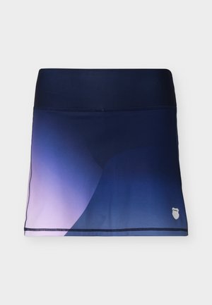 Jupe de sport dégradée bleu marine et violet avec une large ceinture et un petit logo sur l'ourlet en bas à droite, posée à plat sur un fond blanc.