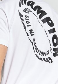 Hvid bomulds t-shirt med stor sort tekst i et spiralmønster, der står "CHAMPION ETABLEREDE I 1919", korte ærmer, rund hals.