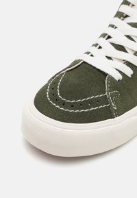 Sneaker verde in suede con lacci bianchi, punta tonda, cuciture decorative e perforazioni sulla parte superiore per la ventilazione.