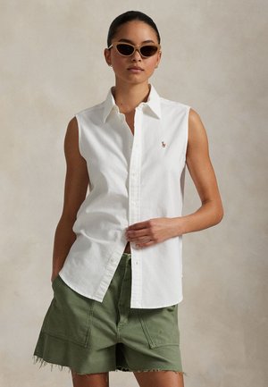 Biela bezrukávová košeľa na gombíky s golierom, s malým logom. Kombinovaná so šortkami olivovo zelenej farby, s voľným strihom a ošúchaným lemom.