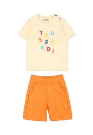 Camicia a maniche corte color crema con lettere colorate sparse e dettaglio con bottone sulla spalla, abbinata a pantaloncini arancioni vivaci con tasche.