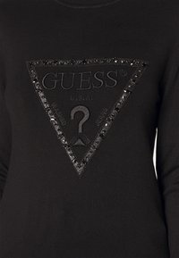 Felpa nera con un logo triangolare strutturato al centro, impreziosito da accenti neri lucidi e dal nome del marchio "GUESS".