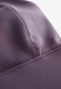 Gorra deportiva morada hecha de un tejido suave y elástico, con costuras planas y una forma estructurada. Primer plano de los detalles de la costura.