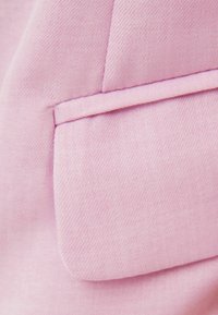 Pink fabric with a smooth texture. Features a pocket with stitched detailing, showcasing a tailored design and clean lines.