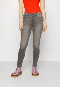 Jeans ajustados grises con una textura suave y un desgaste sutil, combinados con sandalias de tiras color lavanda que presentan una suela de madera gruesa.