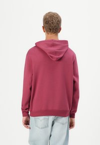 Maroon hoodie with a drawstring hood, ribbed cuffs, and hem, paired with light blue distressed denim jeans, shown from the back.