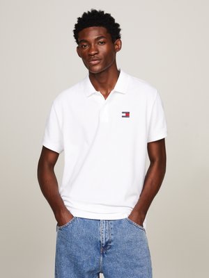 Polo blanco de algodón, con un pequeño logo en el lado izquierdo del pecho. Combinado con jeans de mezclilla azul claro. Ajuste casual con mangas cortas.