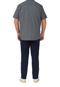 Korte mouw shirt in marineblauw en wit geometrisch patroon, met een ontspannen fit en rugpand. Gecombineerd met donkere broeken en witte sneakers.