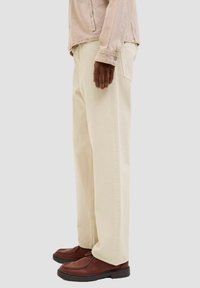 Beige Hosen mit weitem Bein aus Baumwolle, mit glatter Textur und Seitentaschen, kombiniert mit dunkelbraunen Schnürschuhen.