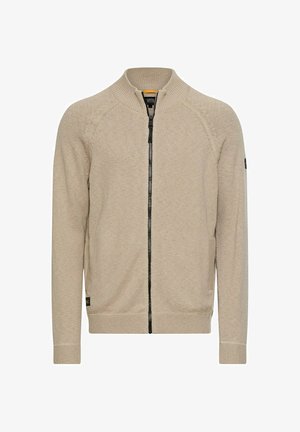 Lysebeige cardigan med lynlås i strikket stof, der har en ribbet krave, sort lynlås og sidelommer. Enkel design uden mønstre.