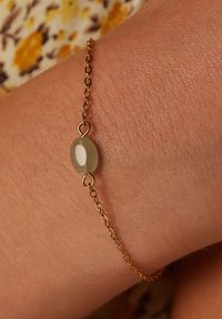 Gouden kettingarmband met een ovale, doorschijnende edelsteen in het midden. De ketting heeft kleine schakels, wat zorgt voor een delicate uitstraling.