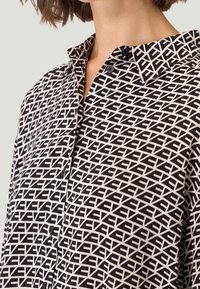 Sort-hvid mønstret skjorte med geometriske designs, klassisk krave og knapdetaljer langs forsiden. Blød stofstruktur.