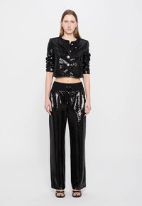Cropped black sequined jacket with two buttons, paired with black sequined wide-leg pants and flat sandals. Smooth texture and shiny finish.