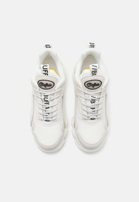 Baskets blanches de sport en maille et en matériau synthétique, avec des patchs de logo noirs, des accents texturés et une semelle blanche épaisse.