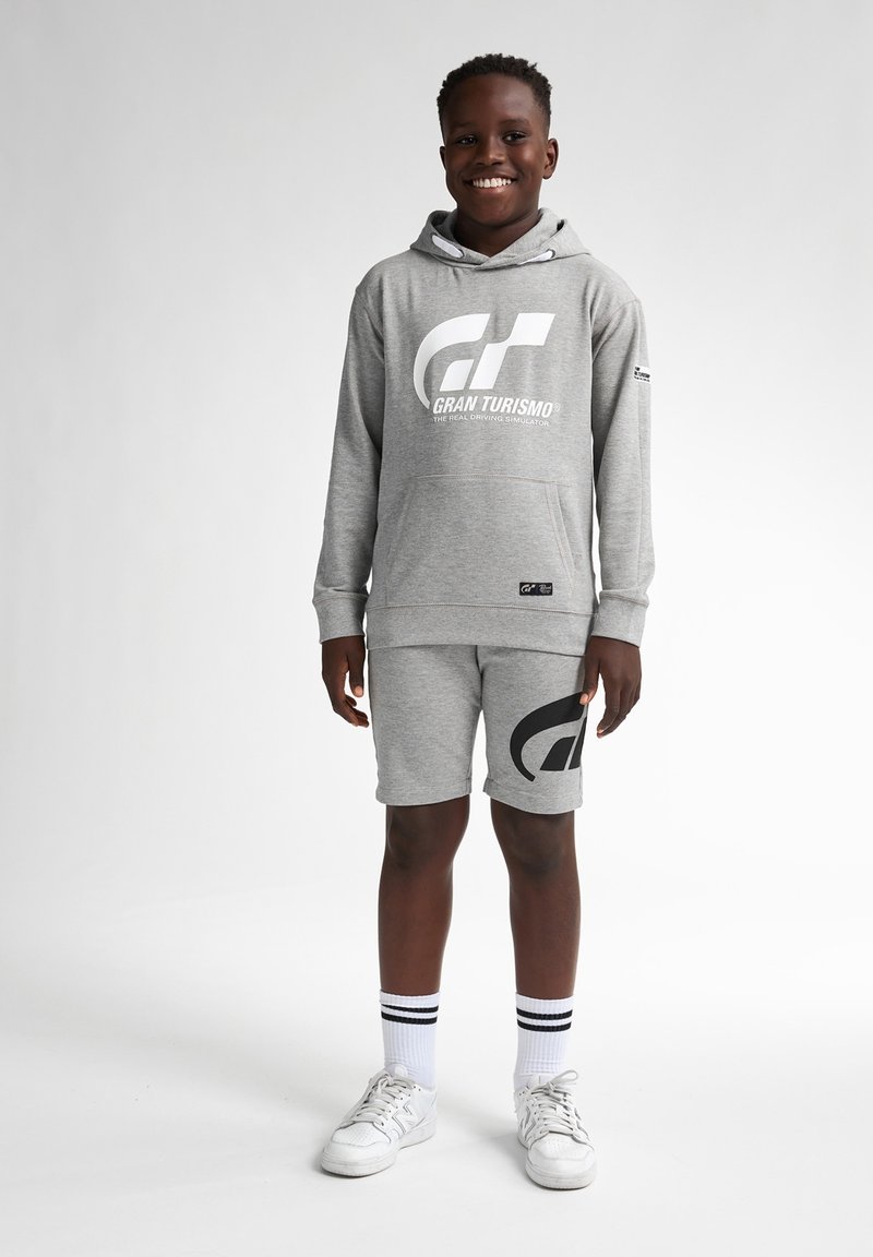 Šedá souprava s mikinou a šortkami, která se pyšní velkým černým logem "GT" a textem. Materiál vypadá jako měkká bavlněná směs; obsahuje kapuci se šňůrkou a kapsy.