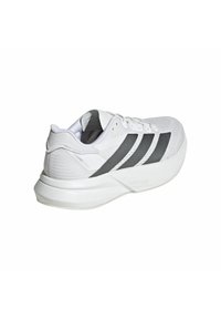 Zapatilla deportiva blanca con rayas negras, parte superior texturizada, suela acolchada y un diseño elegante. Presenta material ligero y cierre con cordones.