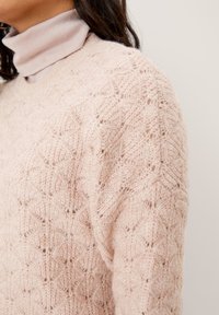 Pull en maille rose clair, avec un motif en losange texturé, un col rond et une coupe légèrement oversize. Le tissu semble doux et aérien.