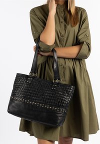 Czarna torba na ramię z plecionki skórzanej z gładkim skórzanym dnem, metalowymi ćwiekami i podwójnymi uchwytami. Torba ma prostokątny kształt i teksturowaną powierzchnię.