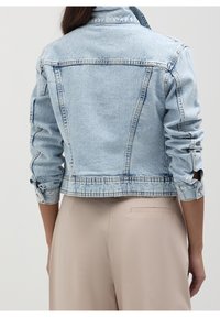 Light blue denim jacket with a cropped design, rolled sleeves, and button accents. Features visible stitching and a classic collar.