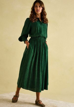 Grünes Kleid mit langen Ärmeln, einem geknöpften Kragen und einem elastischen Bund. Verfügt über einen strukturierten Stoff mit einem dezenten Muster und Seitentaschen.