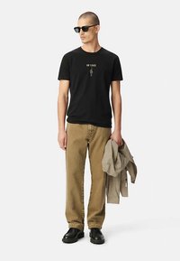 Camiseta negra con gráfico "ON STAGE", pantalones de pana marrón, chaqueta de cuadros gris y zapatos negros. Gafas de sol completan el look.